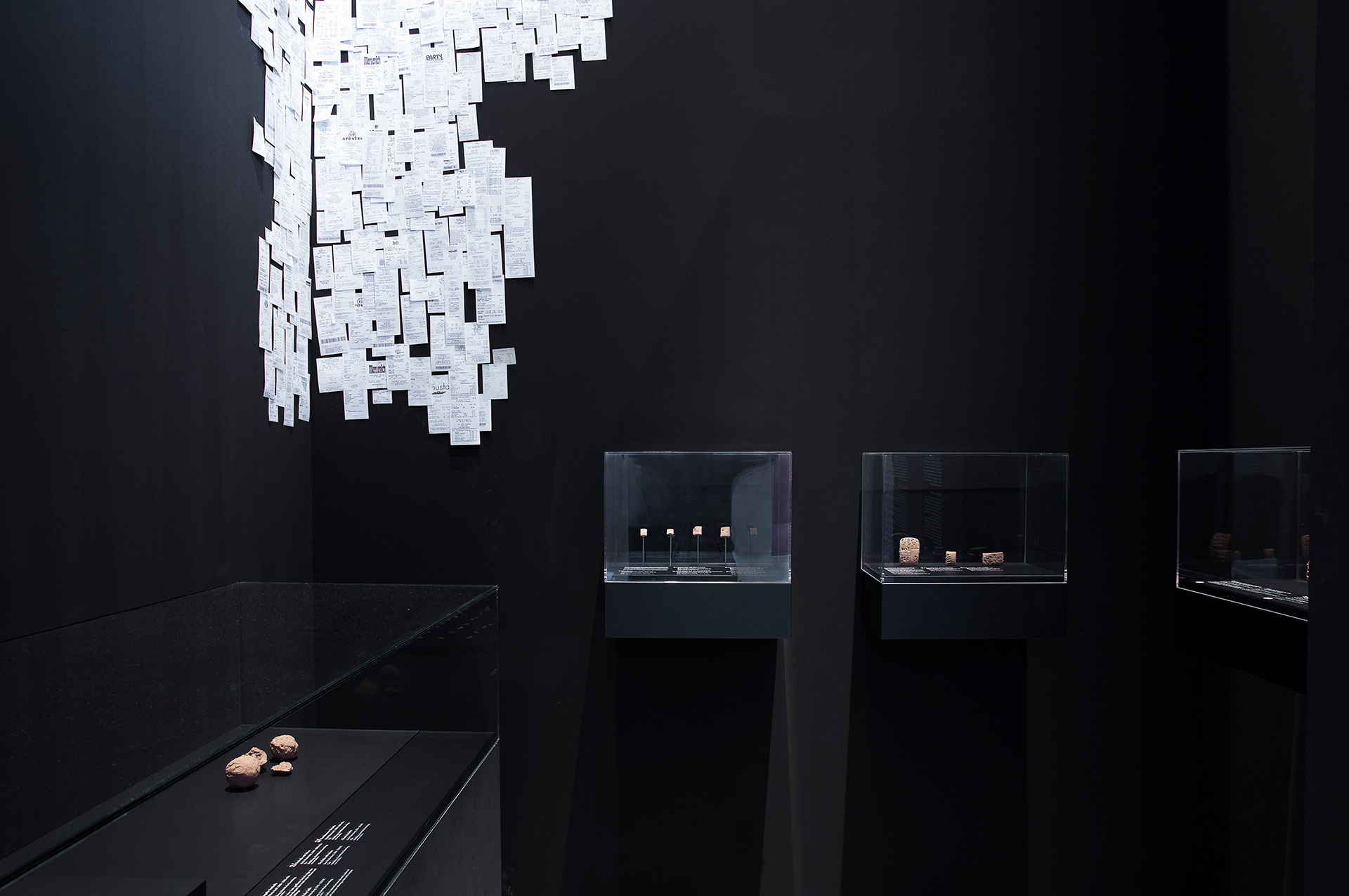 großes Ausstellungsmöbel in Form eines Quaders. Wandfläche läuft nach innen konisch zusammen. Auf den Flächen dazwischen befinden sich Aufsatzvitrinen, Einlassvitrinen und Text