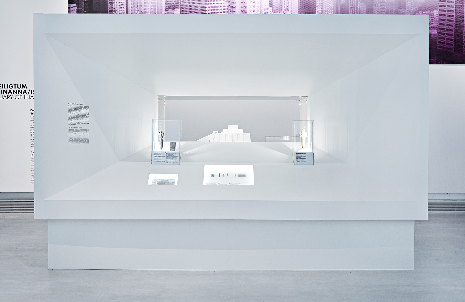 großes Ausstellungsmöbel in Form eines Quaders. Wandfläche läuft nach innen konisch zusammen. Auf den Flächen dazwischen befinden sich Aufsatzvitrinen, Einlassvitrinen und Text