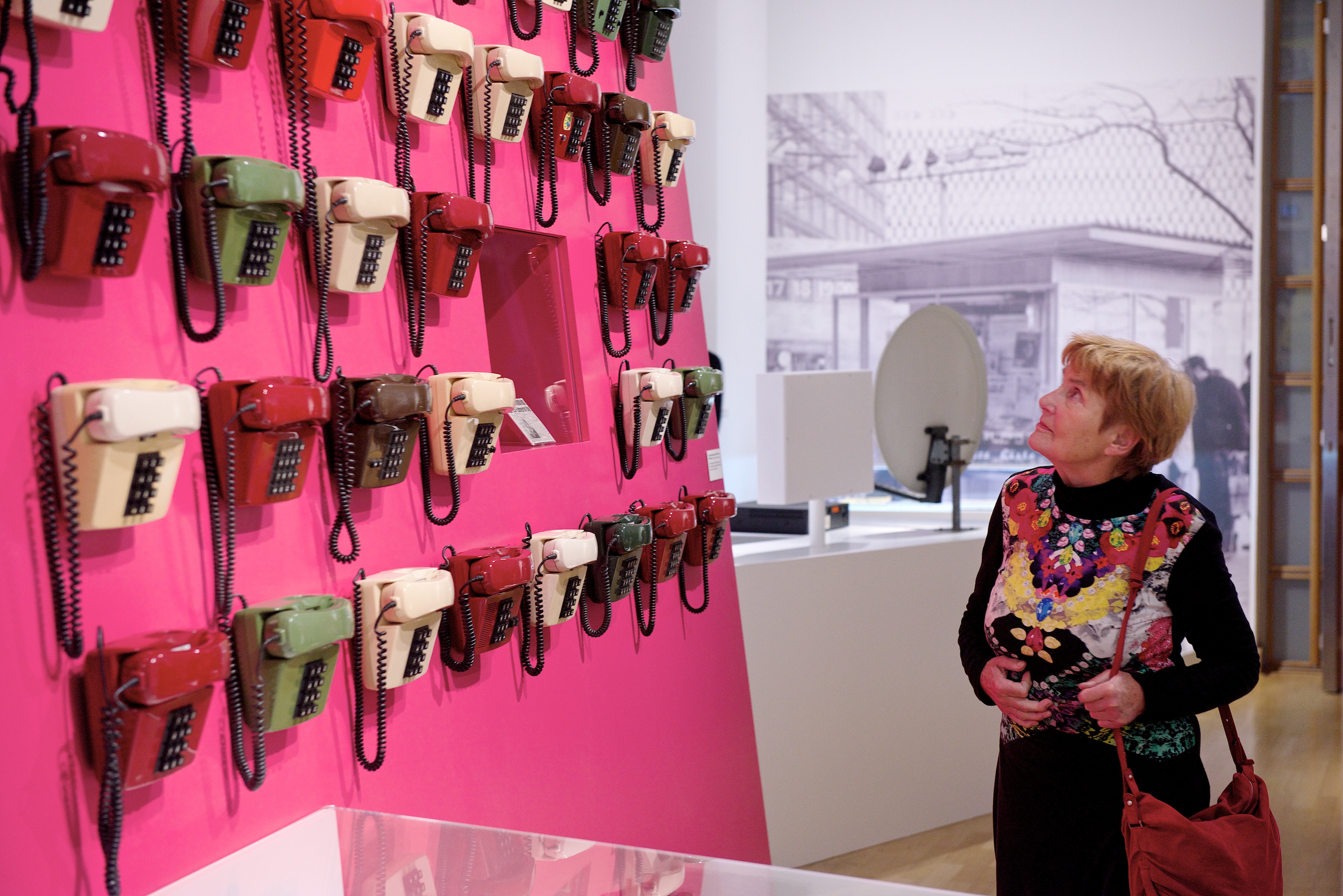 Besucherin betrachtet magenta-farbene Wand mit alten Telefonen darauf