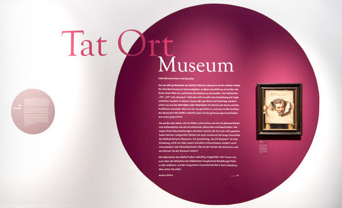rote Kreisgrafik auf Wand mit Text "TatOrt Museum" und gerahmten Bild