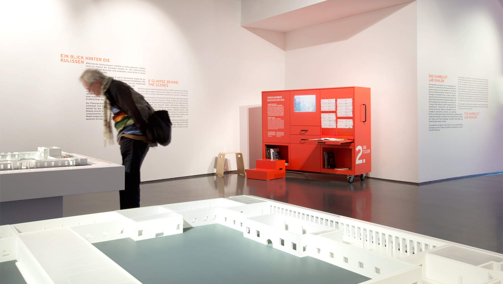 Mobiles rotes Ausstellungsmöbel mit verschiedenen Auszügen, Texten, Fächern für Bücher und einem Monitor