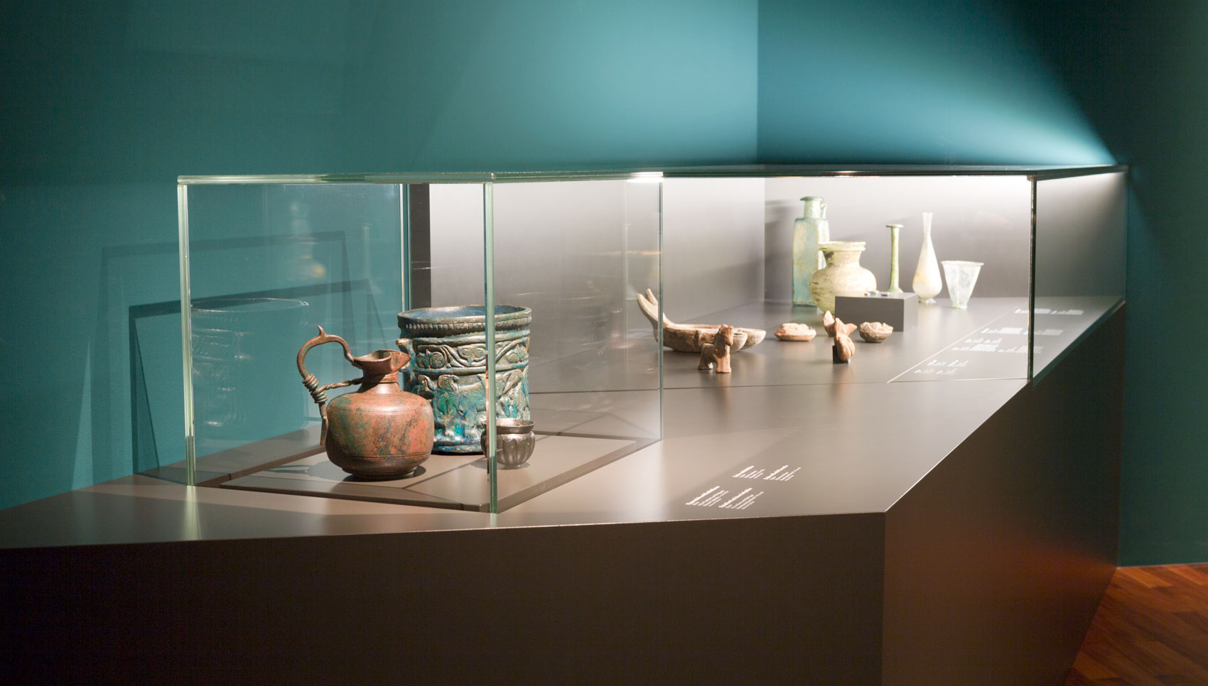 Aufsatzvitrinen auf schwarzem Tischpodest vor petrolfarbener Wand