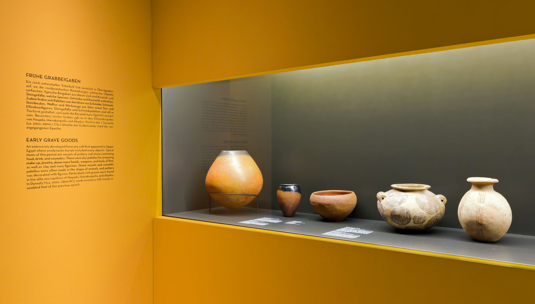 Gelbe Ausstellungswand mit Wandvitrine in der Keramik-Exponate stehen