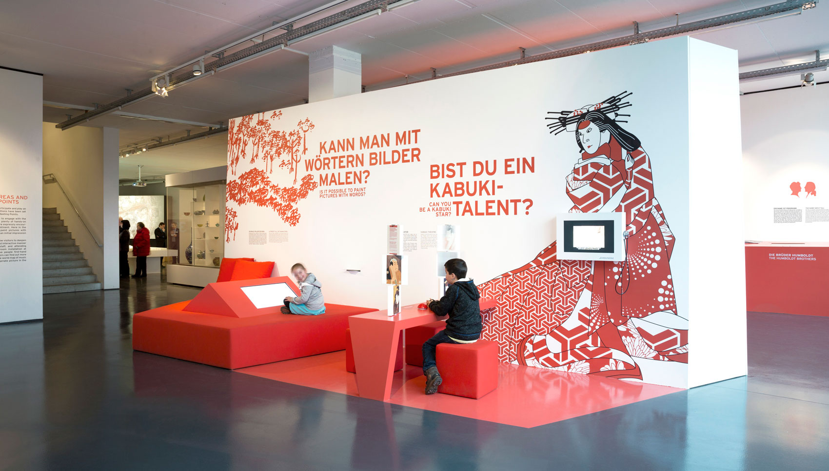 rote Sitzinsel mit Medienstation auf der zwei Kinder sitzen und damit interagieren