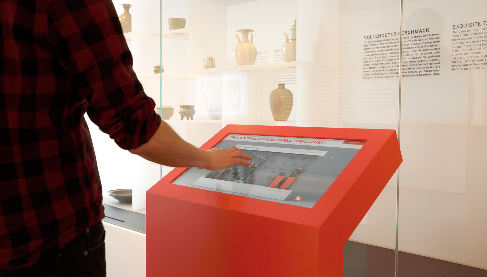 Besucher interagiert mit Medienterminal "Ein chinesisches Kostbarkeitenkabinett" vor großer Schrankvitrine