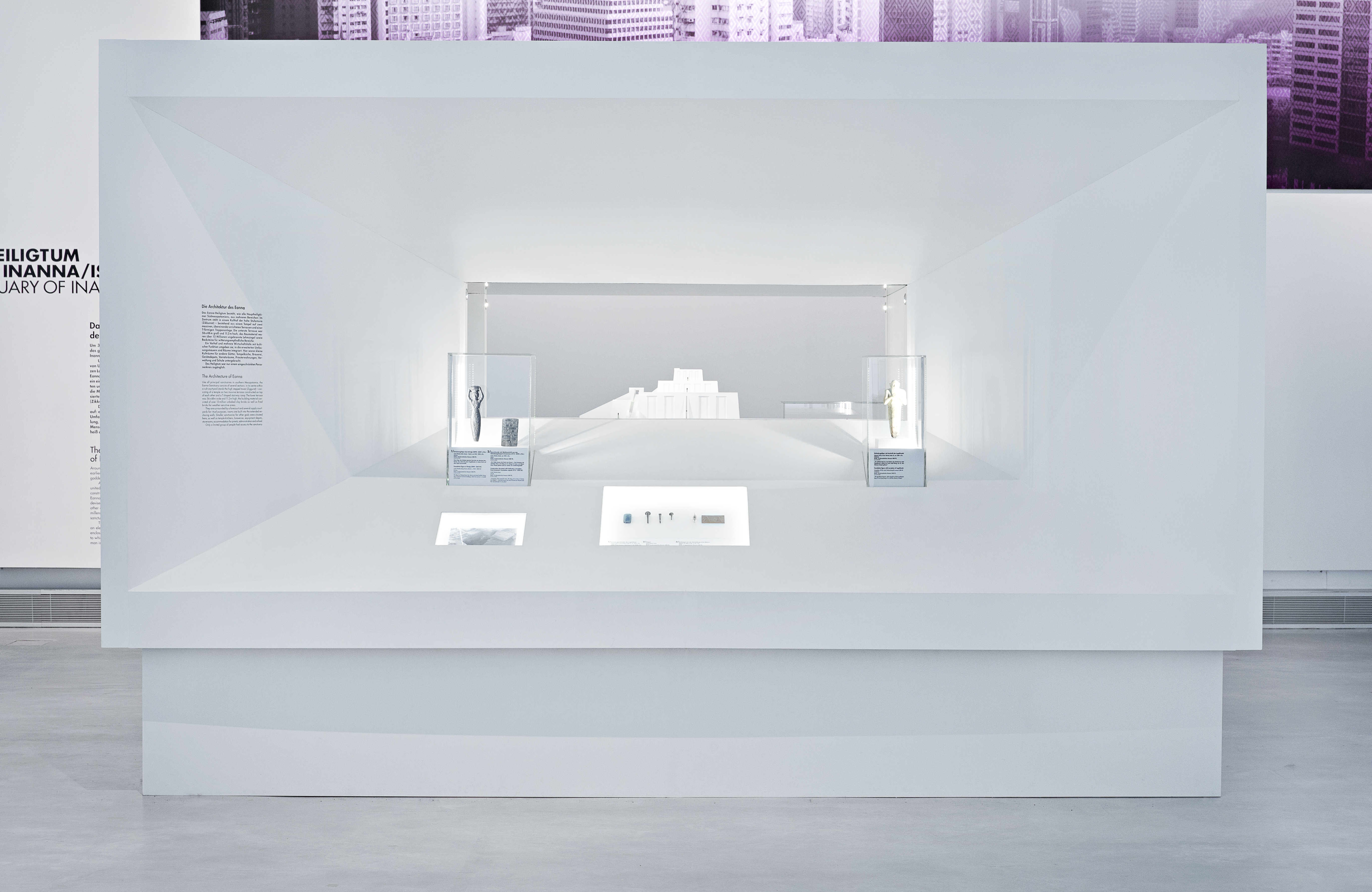 großes Ausstellungsmöbel in Form eines Quaders. Wandfläche läuft nach innen konisch zusammen. Auf den Flächen dazwischen befinden sich Aufsatzvitrinen, Einlassvitrinen und Text