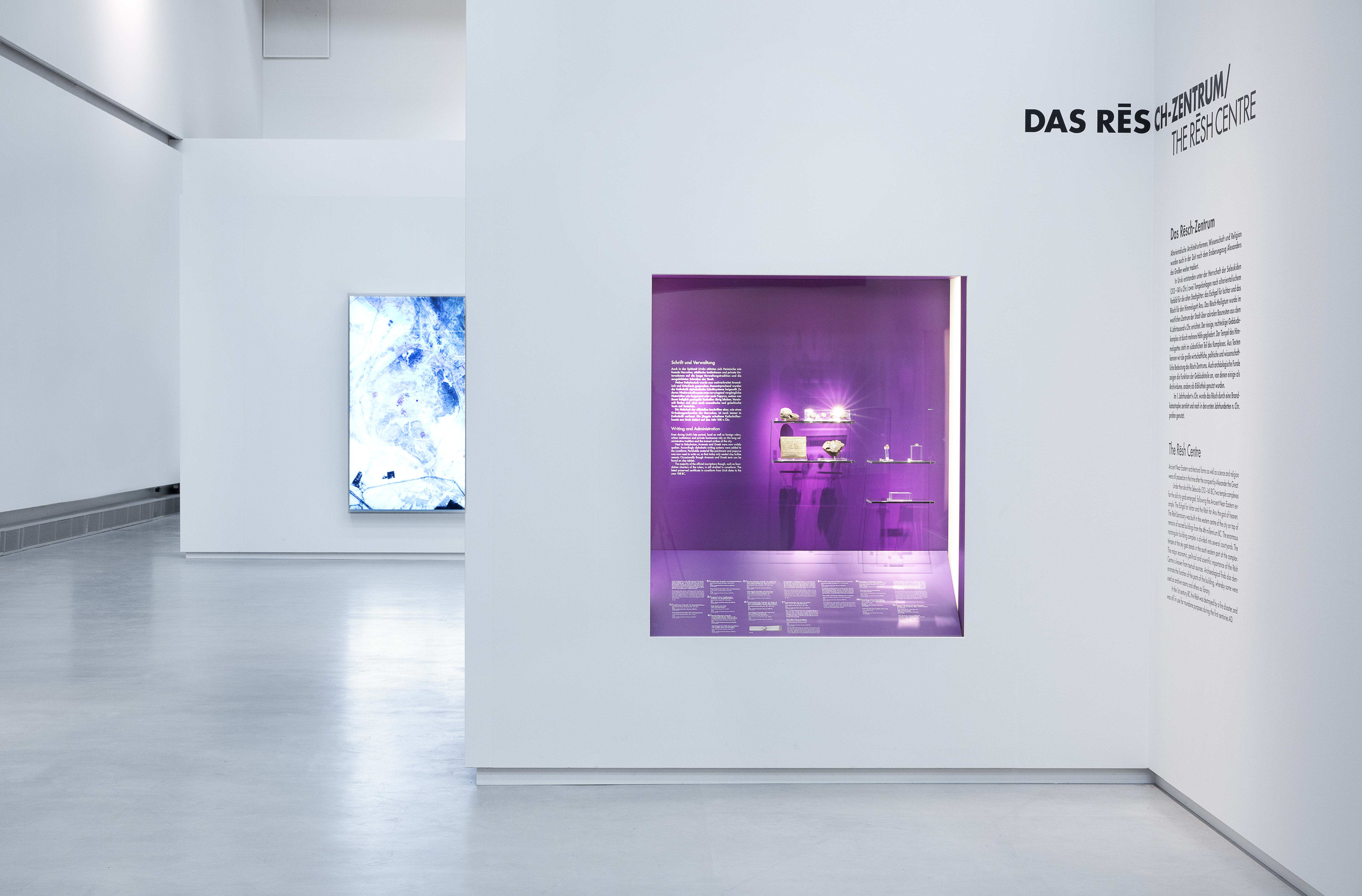 weiße Ausstellungswand mit Wandvitrine, die sich durch violette Rückwand abhebt