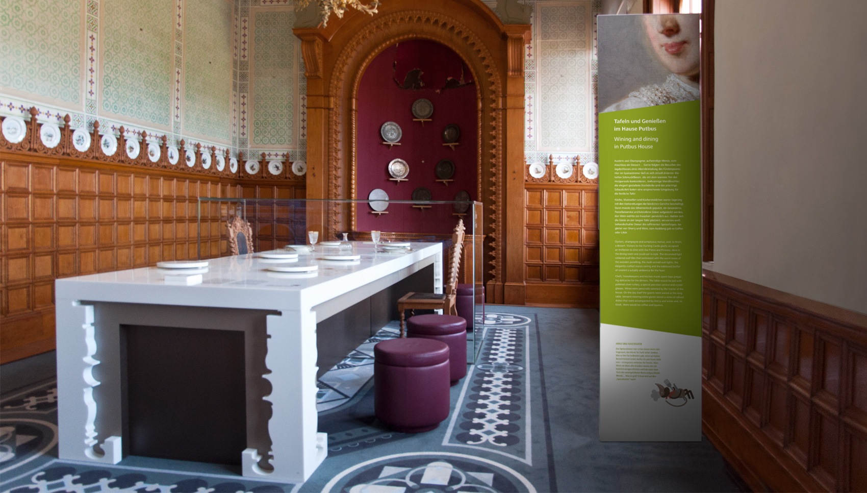 Raum mit nachgebauter Esstafel und verglastem Bereich unter dem sich Original Esstisch Exponate befinden. Daneben Stehpaneel mit Beschriftung "Tafeln und Genießen"