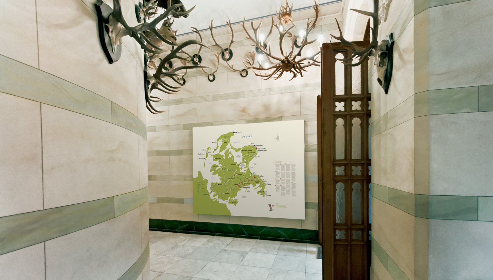 Blick in Marmorgang mit Informationsgrafik auf davor befestigter Tafel, darüber verschiedene Geweihe.