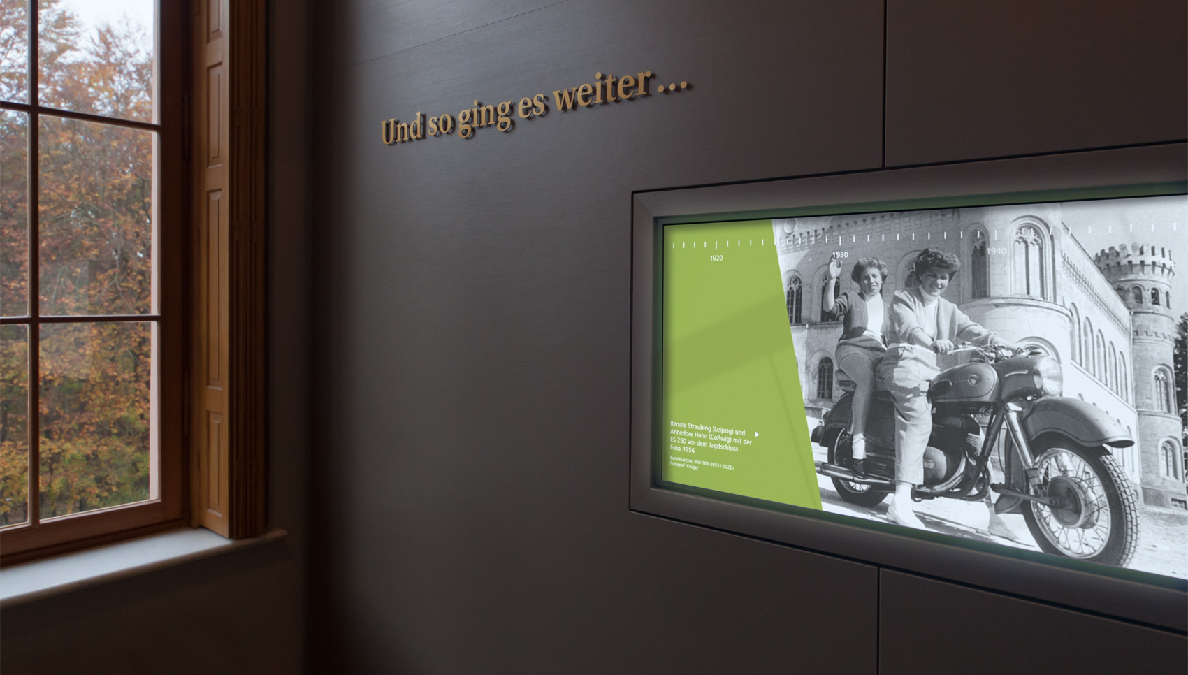 Blick auf dunkelbraune Holzvertäfelung mit Schriftzug "Und so ging es weiter.." darunter schwarz-weiß Fotografie zweier Frauen auf einem Motorrad und darüber befindlichen Zeitstrahl beginnend 1915