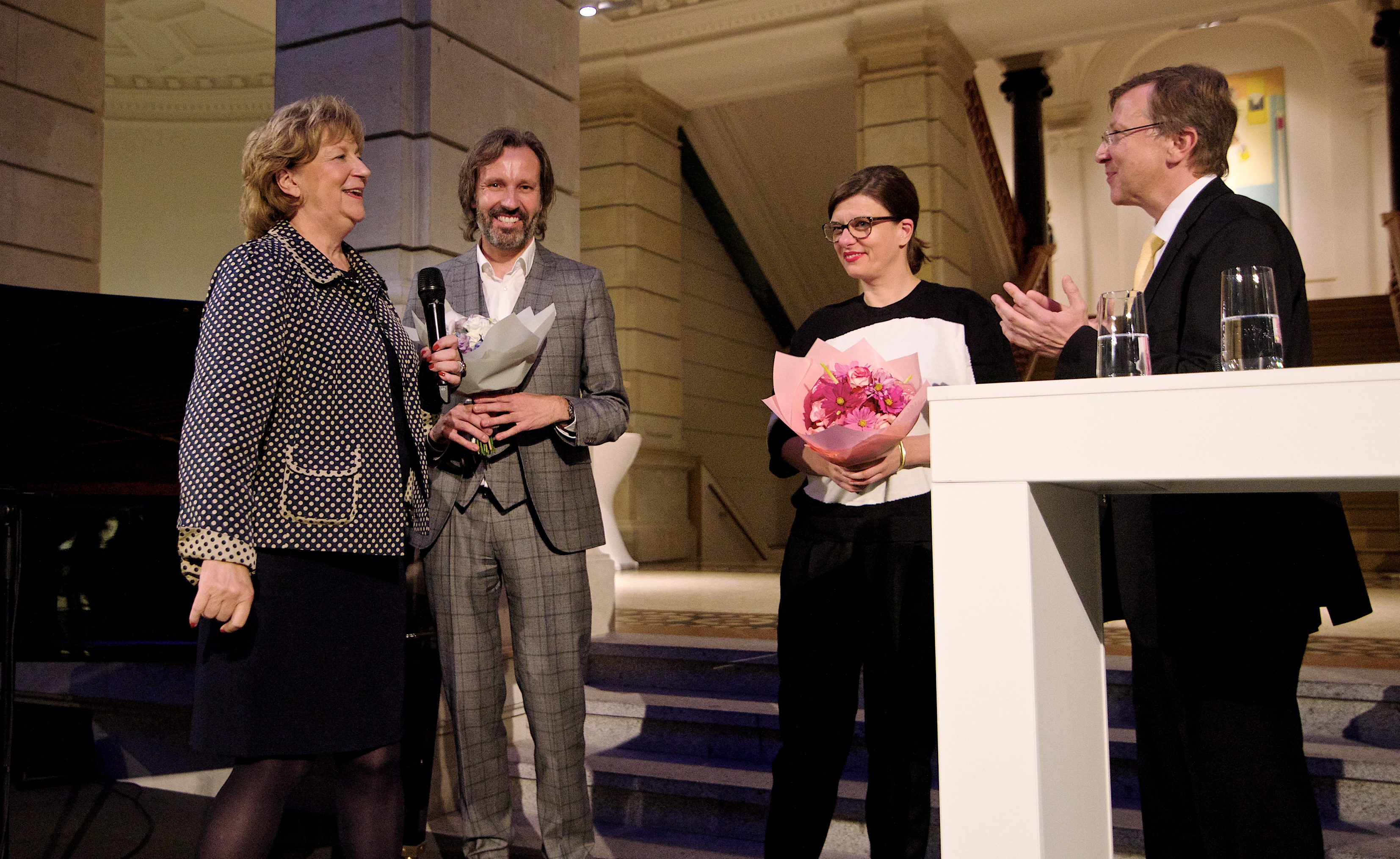Ingo Plato und Rebecca Schröder bekommen auf der Bühne Blumenstrauß überreicht