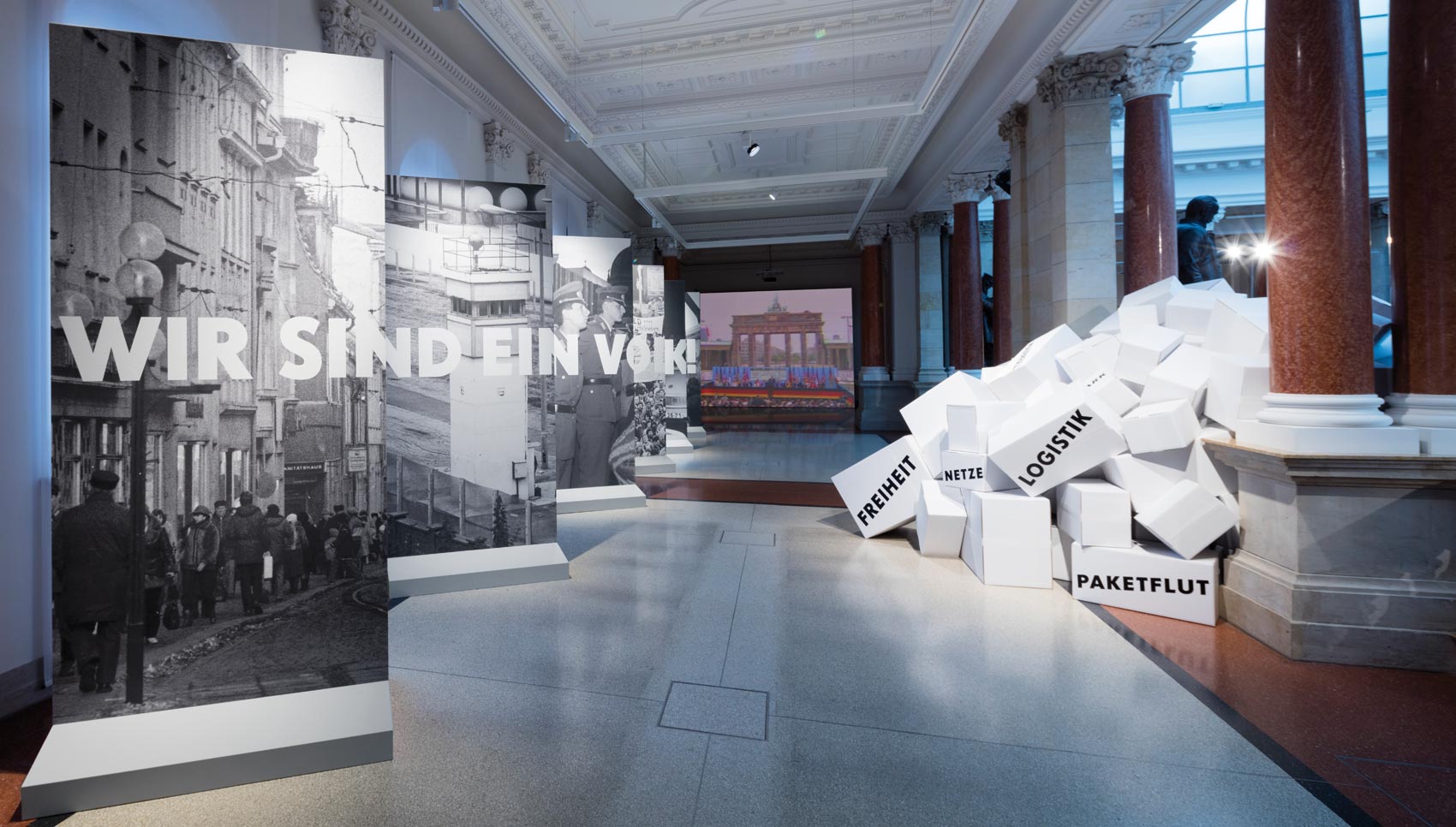 Raum Installation mit Berliner-Mauer ähnlichen Ausstellungswänden, die bedruckt sind mit Fotografik und Text "Wir sind ein Volk!"