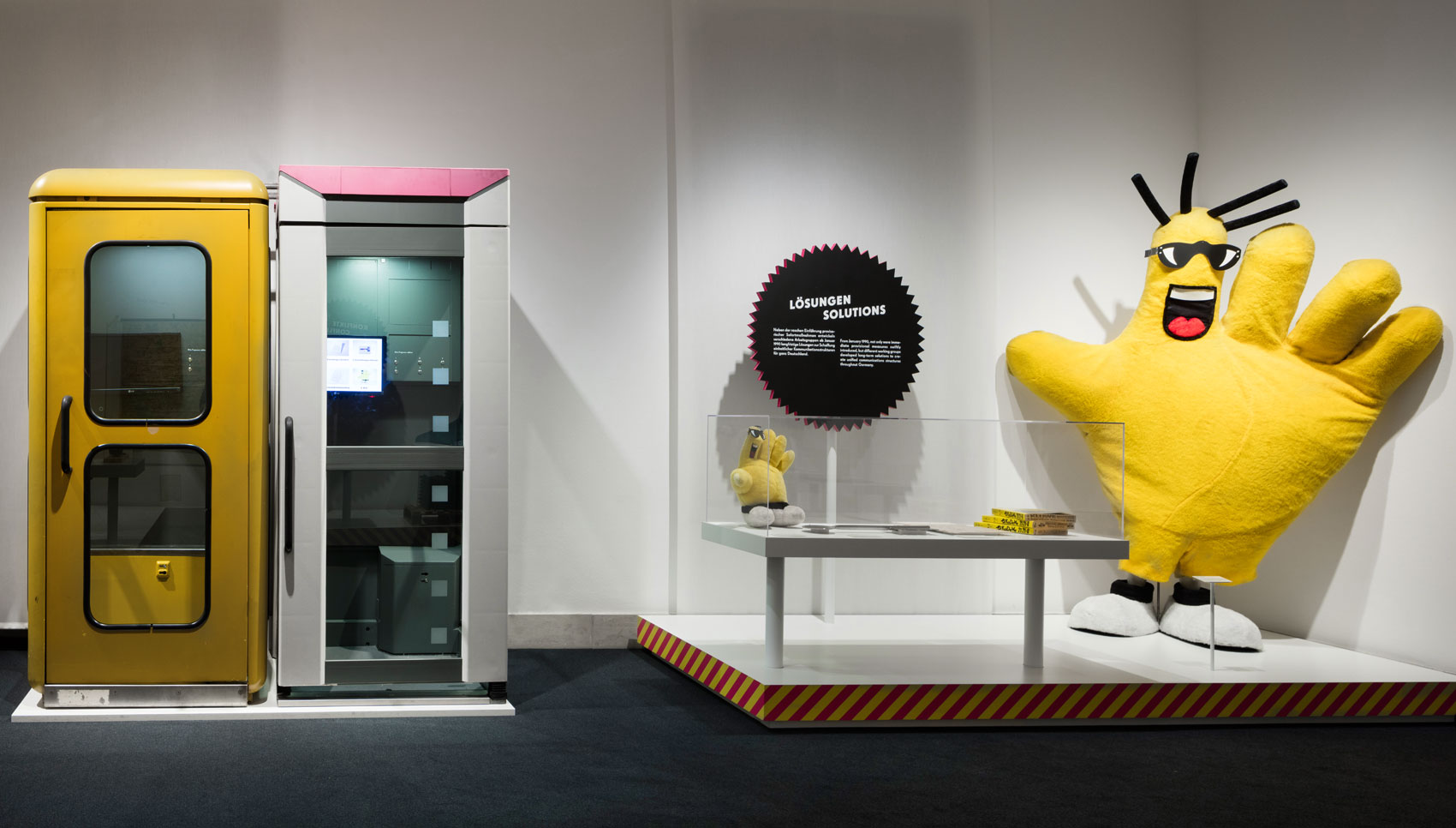 Links zwei unterschiedliche Telefonzellen. Rechts großer gelber Handschuh mit Gesicht und Text "Lösungen"