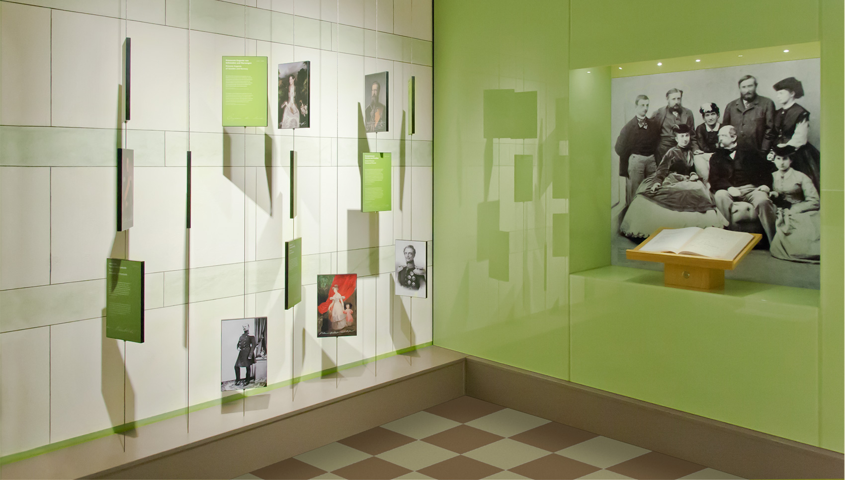 Blick auf grüne Wand und Wandvitrine mit aufgeschlagenem Buch und schwarz-weiß Fotografie einer Familie darüber