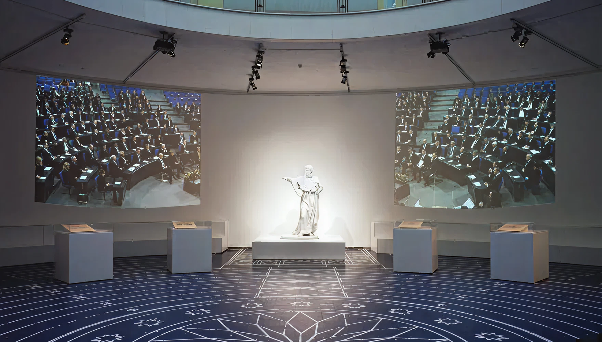 Blick auf eine weiße Statue. Daneben, auf beiden Seiten, Projektionen vom Innenraum des Deutschen Bundestags.