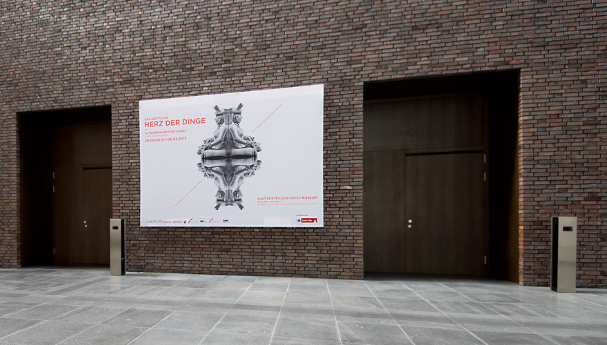 Backsteinwand mit großem Ausstellungsplakat "Das göttliche Herz der Dinge"