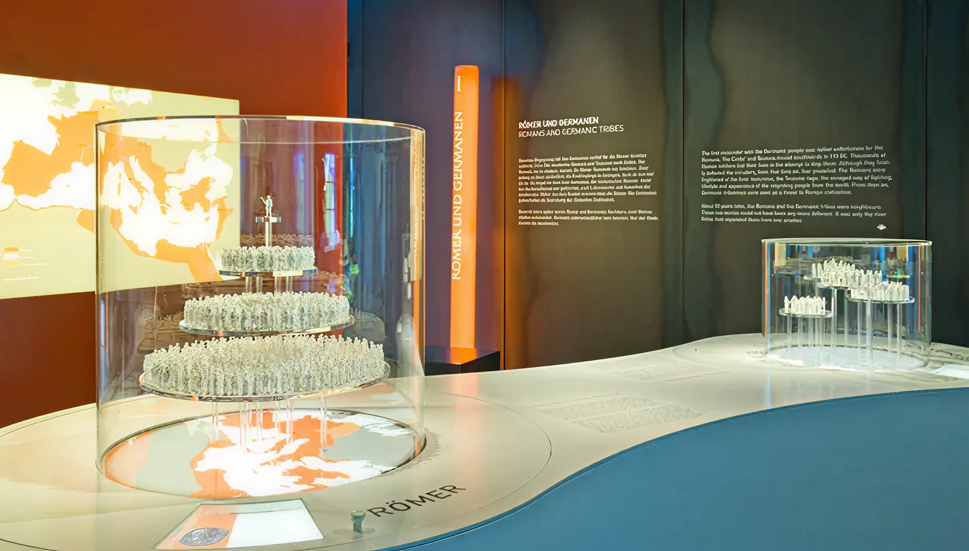 weißes Tischpodest mit zwei runden Aufsatzvitrinen in denen sich kleine weiße Figuren befinden