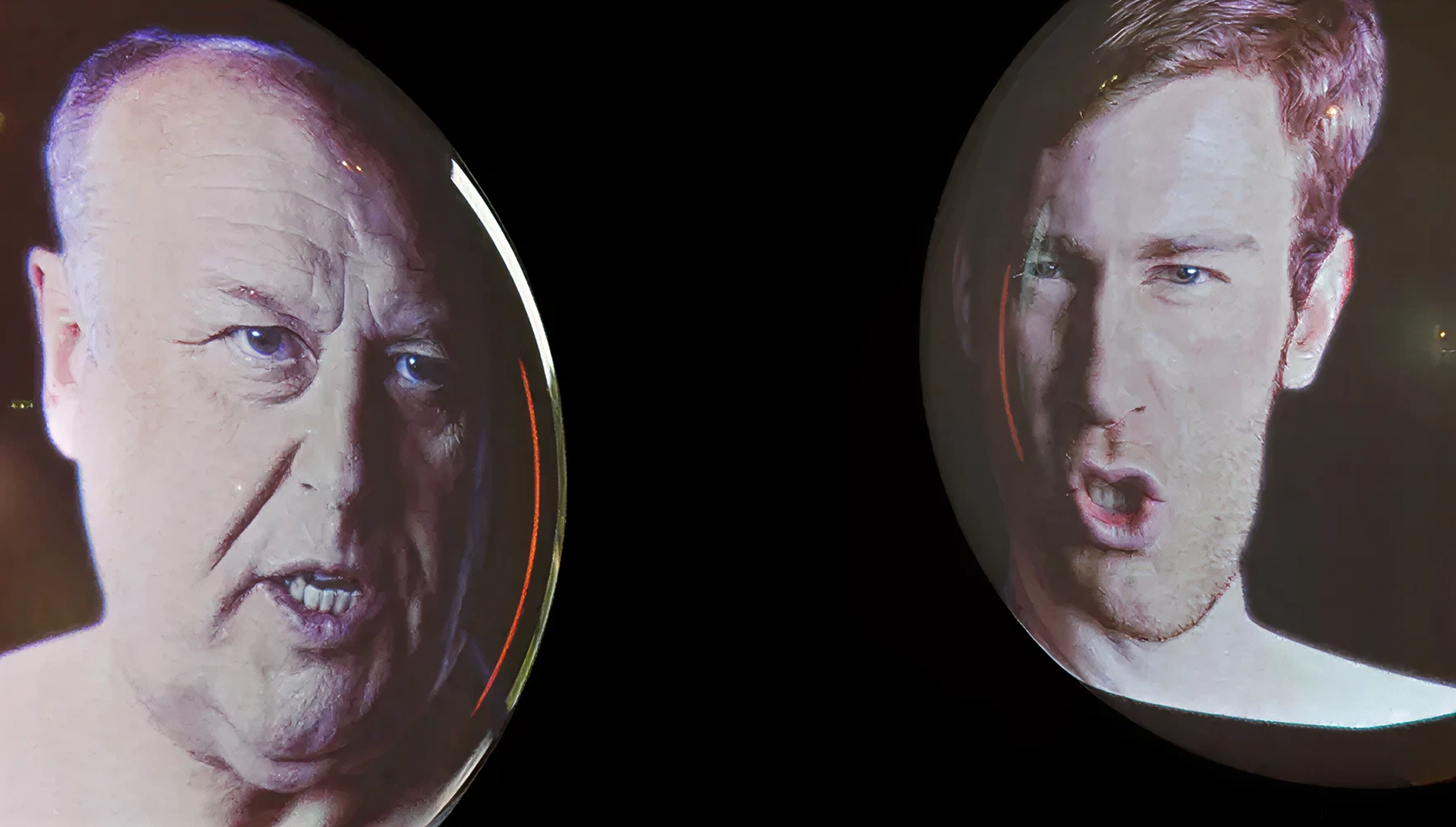 Zwei runde Kugeln vor schwarzer Wand, auf denen sich jeweils eine Projektion eines modernen, männlichen Porträts befindet.