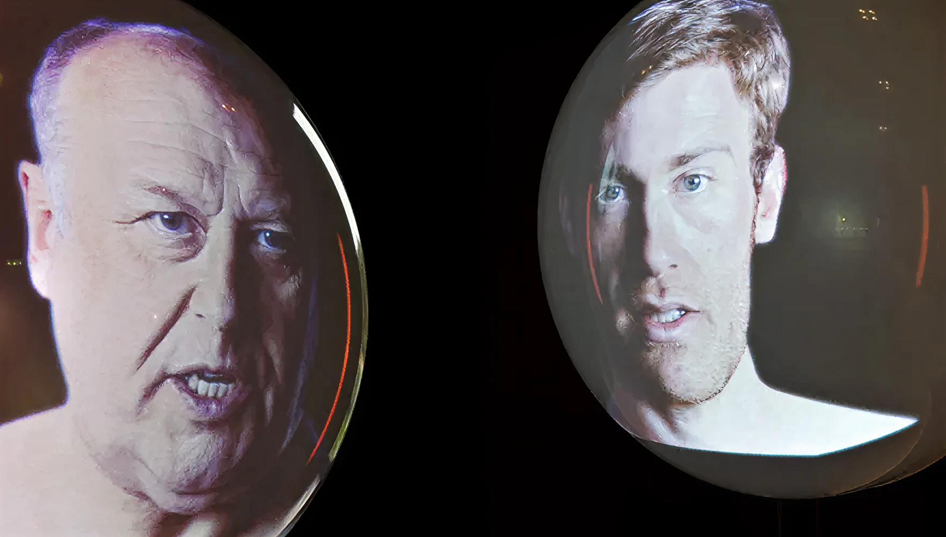 Zwei runde Kugeln vor schwarzer Wand, auf denen sich jeweils eine Projektion eines modernen, männlichen Porträts befindet.