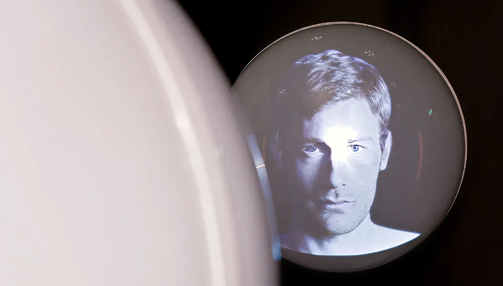 Eine runde Kugeln vor schwarzer Wand, auf denen sich eine Projektion eines modernen, männlichen Porträts befindet.