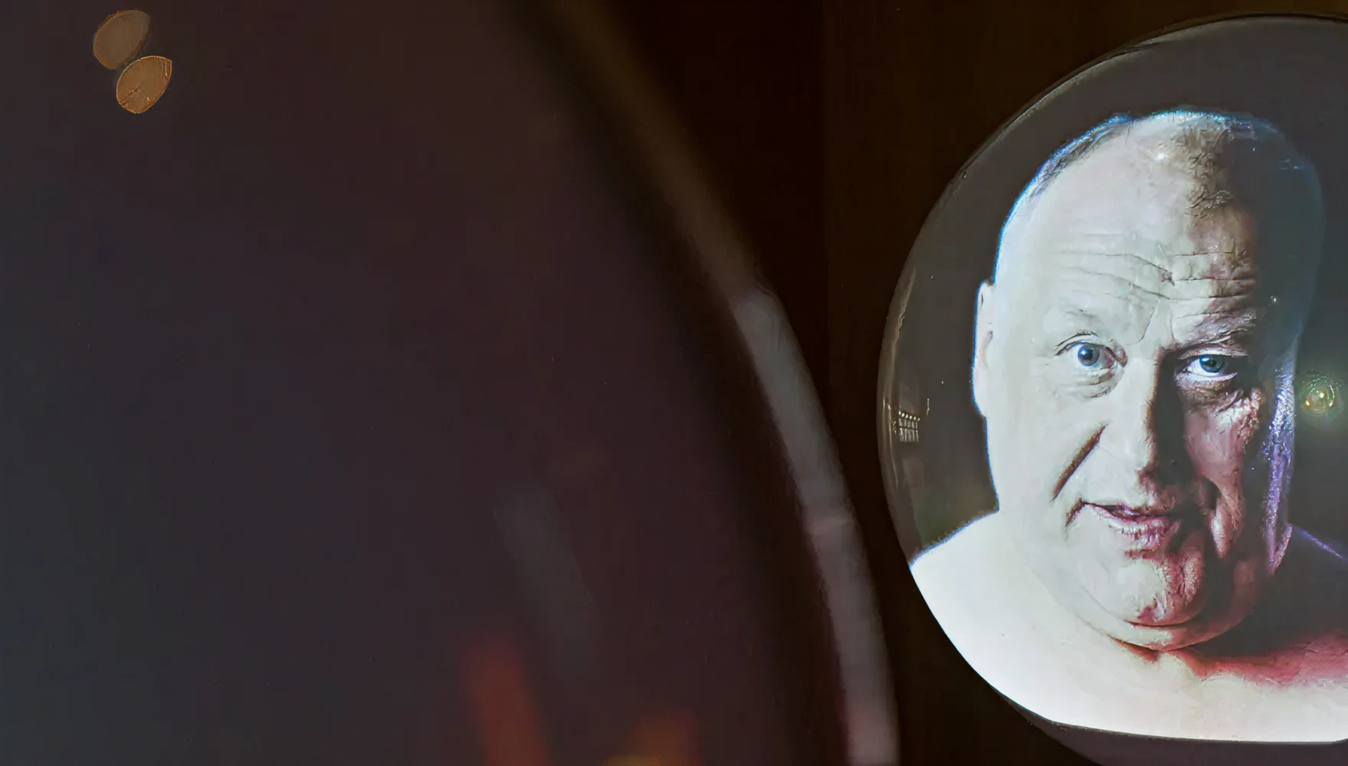 Eine runde Kugeln vor schwarzer Wand, auf denen sich eine Projektion eines modernen, männlichen Porträts befindet.