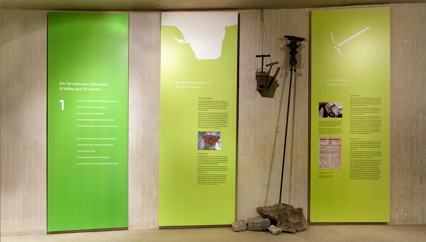 Blick auf Wand mit drei deckenhohen, grünen Paneelen, auf denen Bilder und Text zu sehen sind.