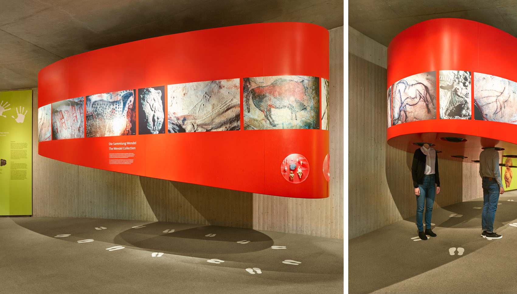 Sehr großes, rotes, ovales Möbel, das von der Decke abhängt und ringsherum Fotos von Höhlenmalereien besitzt. 2 Personen stehen darunter, und ihr Kopf steckt in Löchern. Sie schauen sich etwas im Inneren des Möbels an.