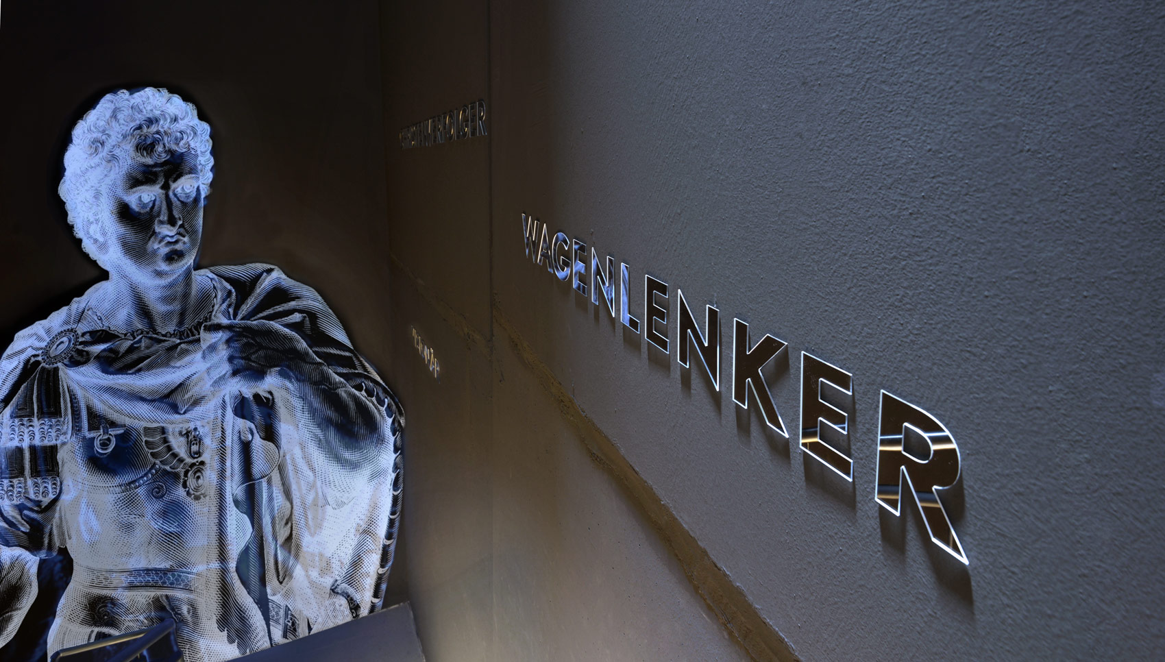 Text "Wagenlenker" an Wand. Buchstaben aus verspiegeltem Acryl