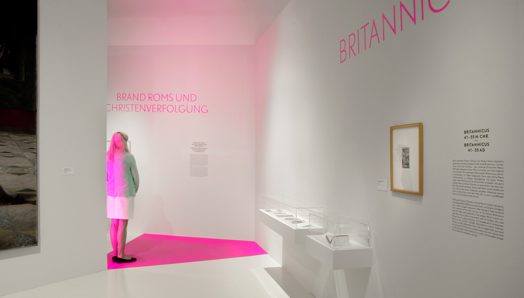 Besucherin steht vor pink hinterleuchtetem Wandobjekt und liest Text