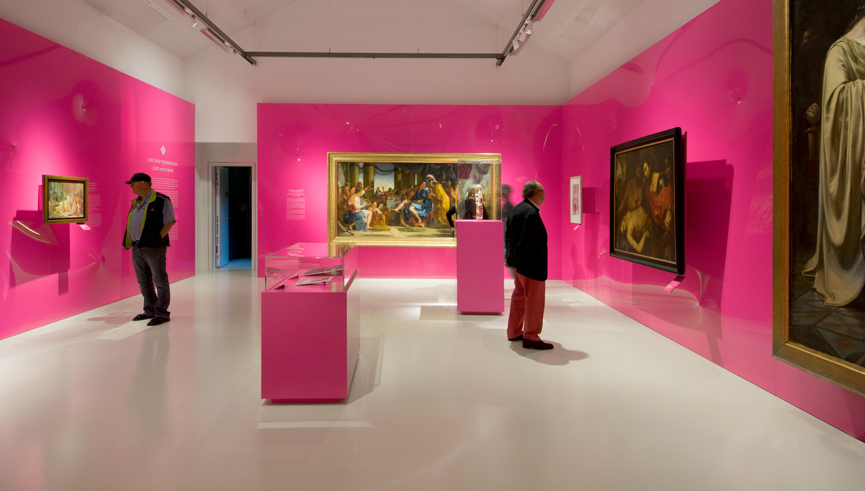 Ausstellungsraum mit pinken Wänden vor denen große gerahmte Gemälde hängen