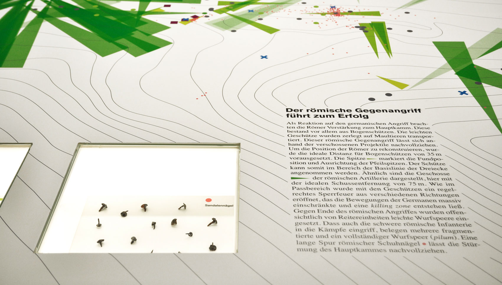 Nahaufnahme einer Einlassvitrine mit Sandalennägeln. Daneben ein Text mit dem Titel "Der römische Gegenangriff führt zum Erfolg"