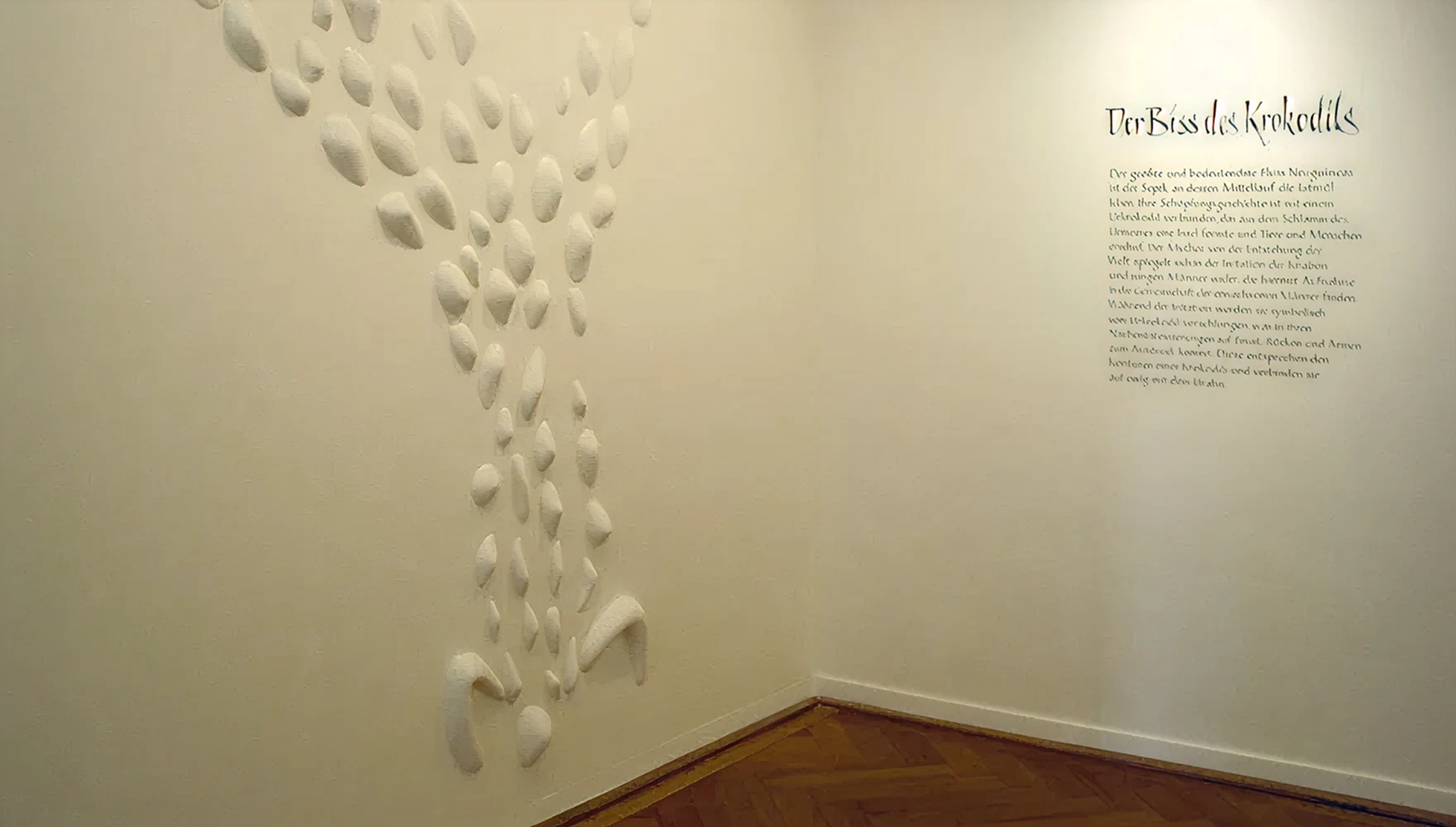 Weiße Wand mit plastischem Muster neben Text "Der Biss des Krokodils"