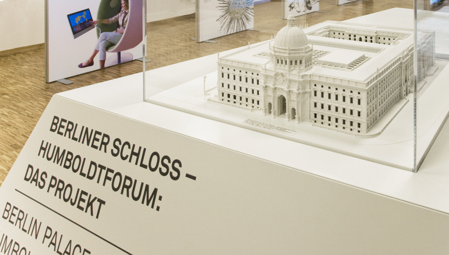 weißes Ausstellungspodest mit schwarzer Schrift "Berliner Schloss – Humboldtforum: das Projekt". Darauf eine Aufsatzvitrine mit einem Weißmodell des Berliner Schlosses