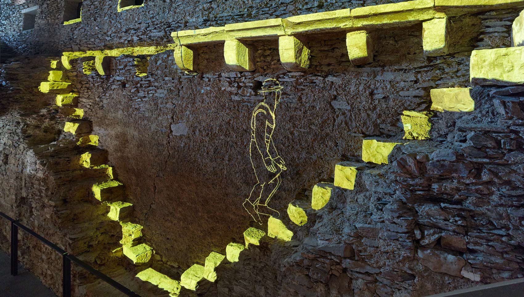 Gelb-leuchtende Projektion auf eine dunkle Burgmauer