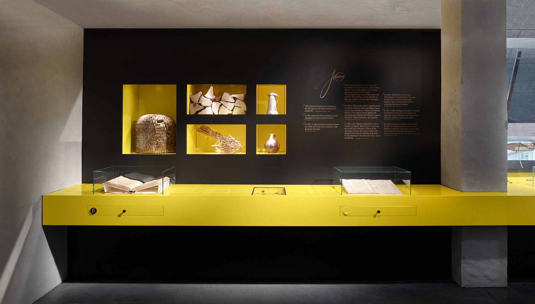 Schwarzes Ausstellungsmöbel mit gelb-leuchtenden Akzenten und verschiedenen Exponaten