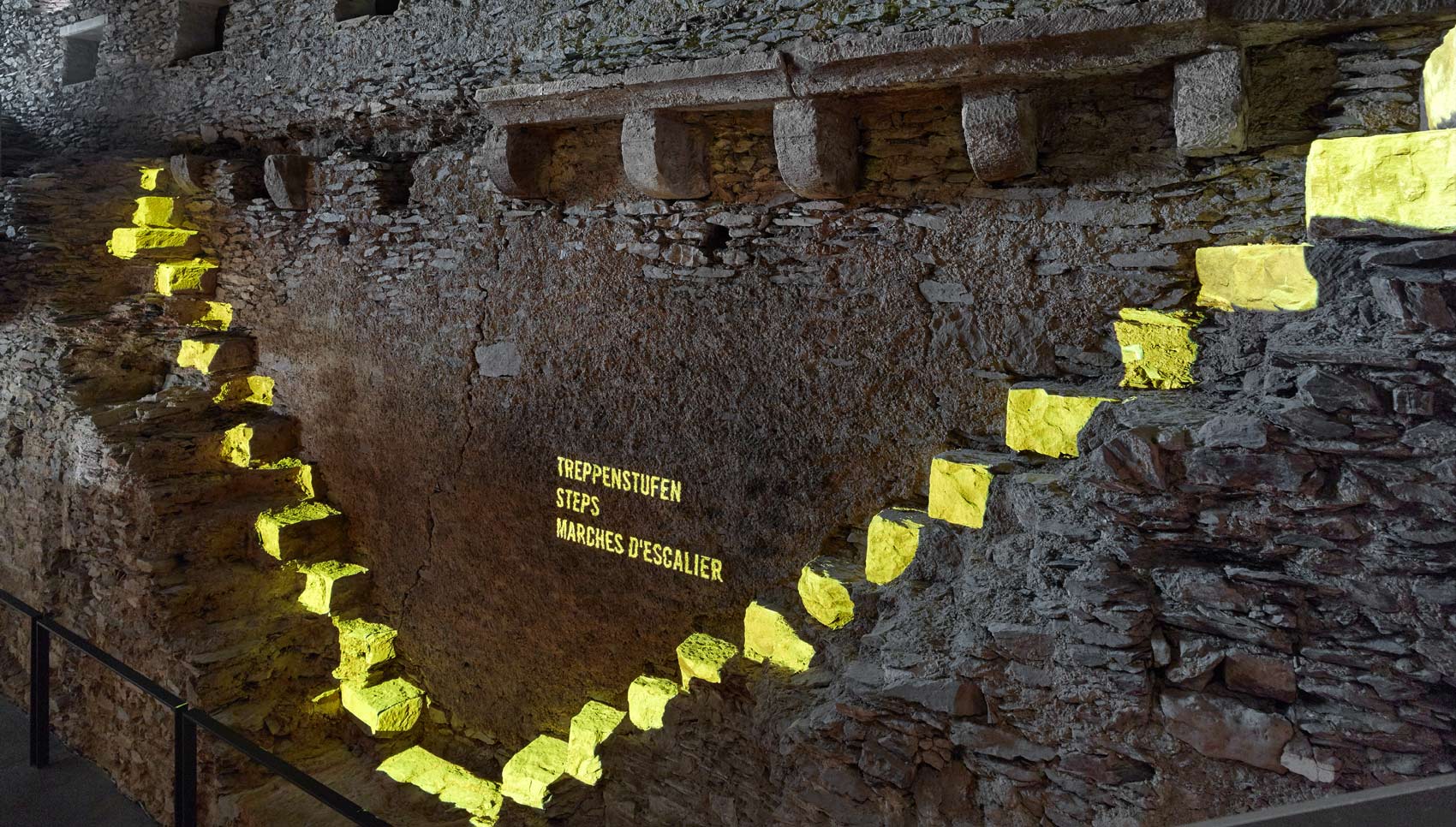 Gelb-leuchtende Projektion auf eine dunkle Burgmauer