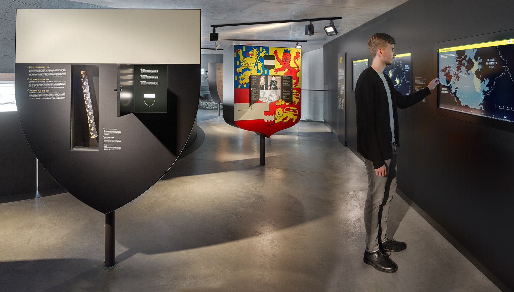 Mann steht im Ausstellungsraum vor interaktiven, in die Wand eingelassenen Touchscreen