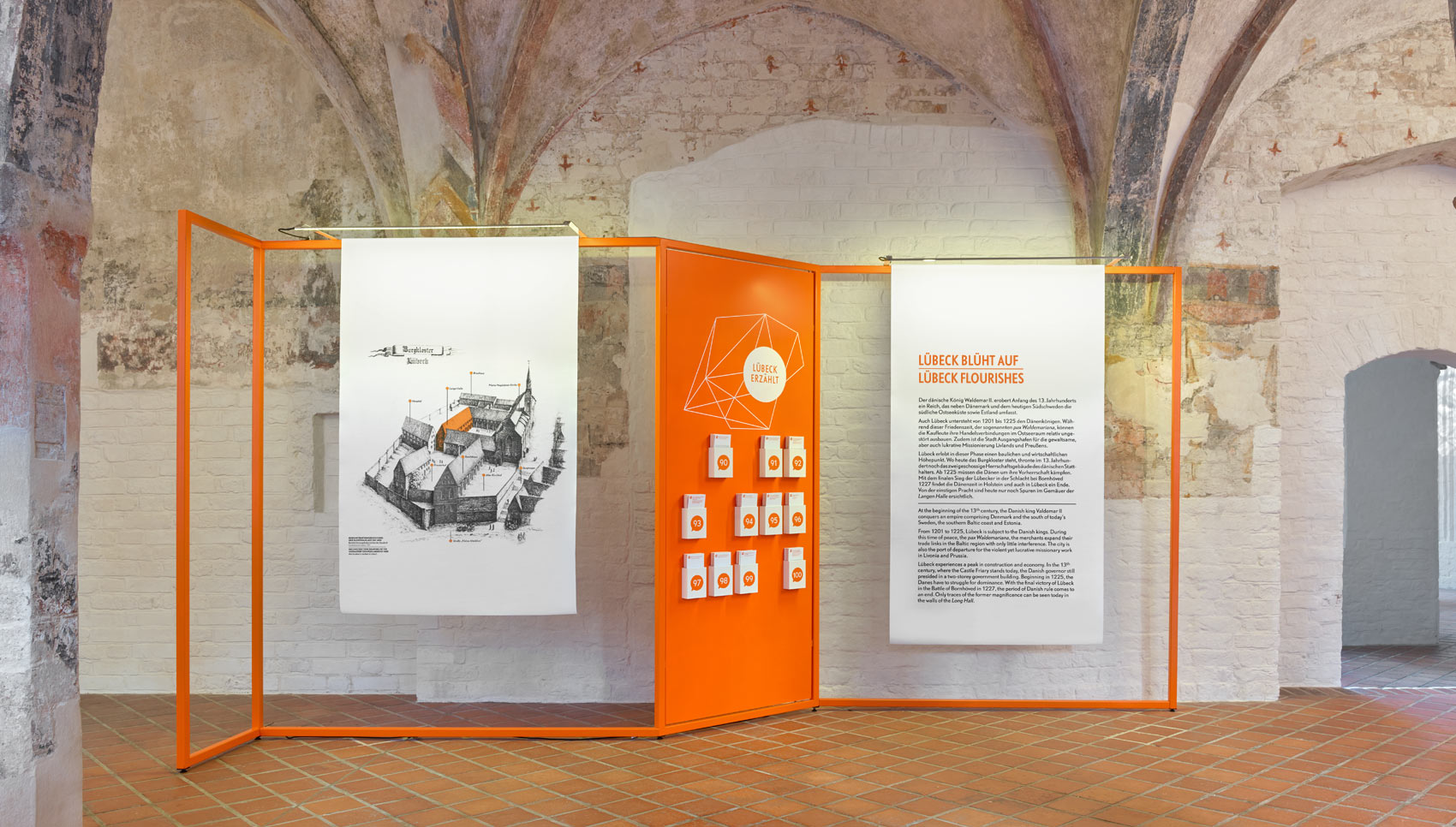 Ausstellungsraum mit Ausstellungsmöbel, bei dem Stoffbanner auf organgefarbigen Stangen hängen