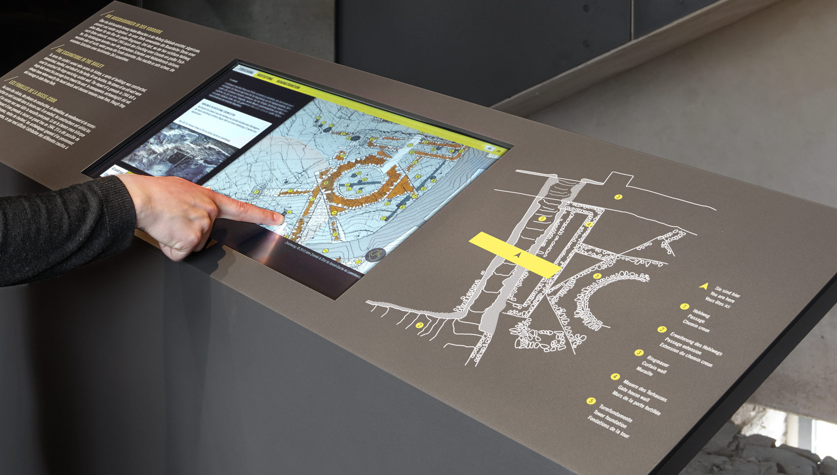 Detailansicht eines Touchscreens mit Ausstellungsgrafiken, der gerade bedient wird