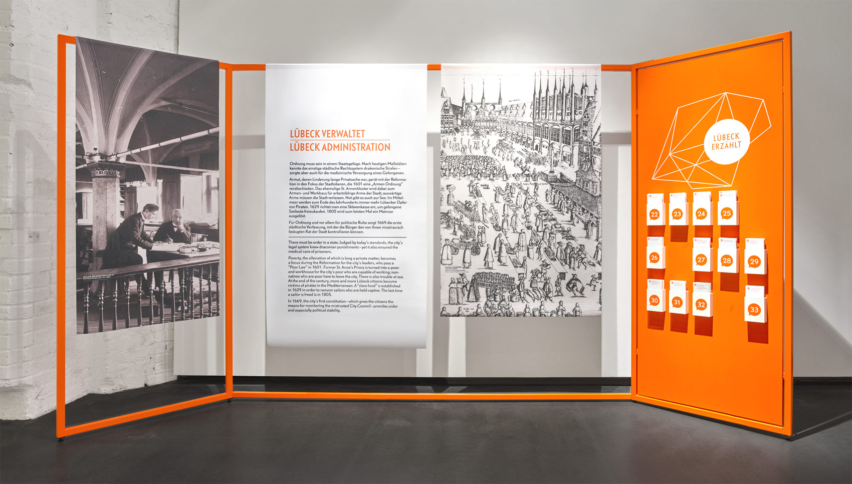 Ausstellungsraum mit Ausstellungsmöbel, bei dem Stoffbanner auf organgefarbigen Stangen hängen