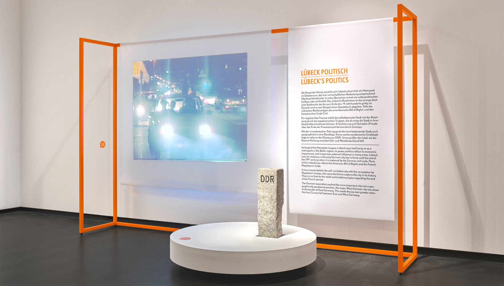 Ausstellungsraum mit Ausstellungsmöbel, bei dem Stoffbanner auf organgefarbigen Stangen hängen