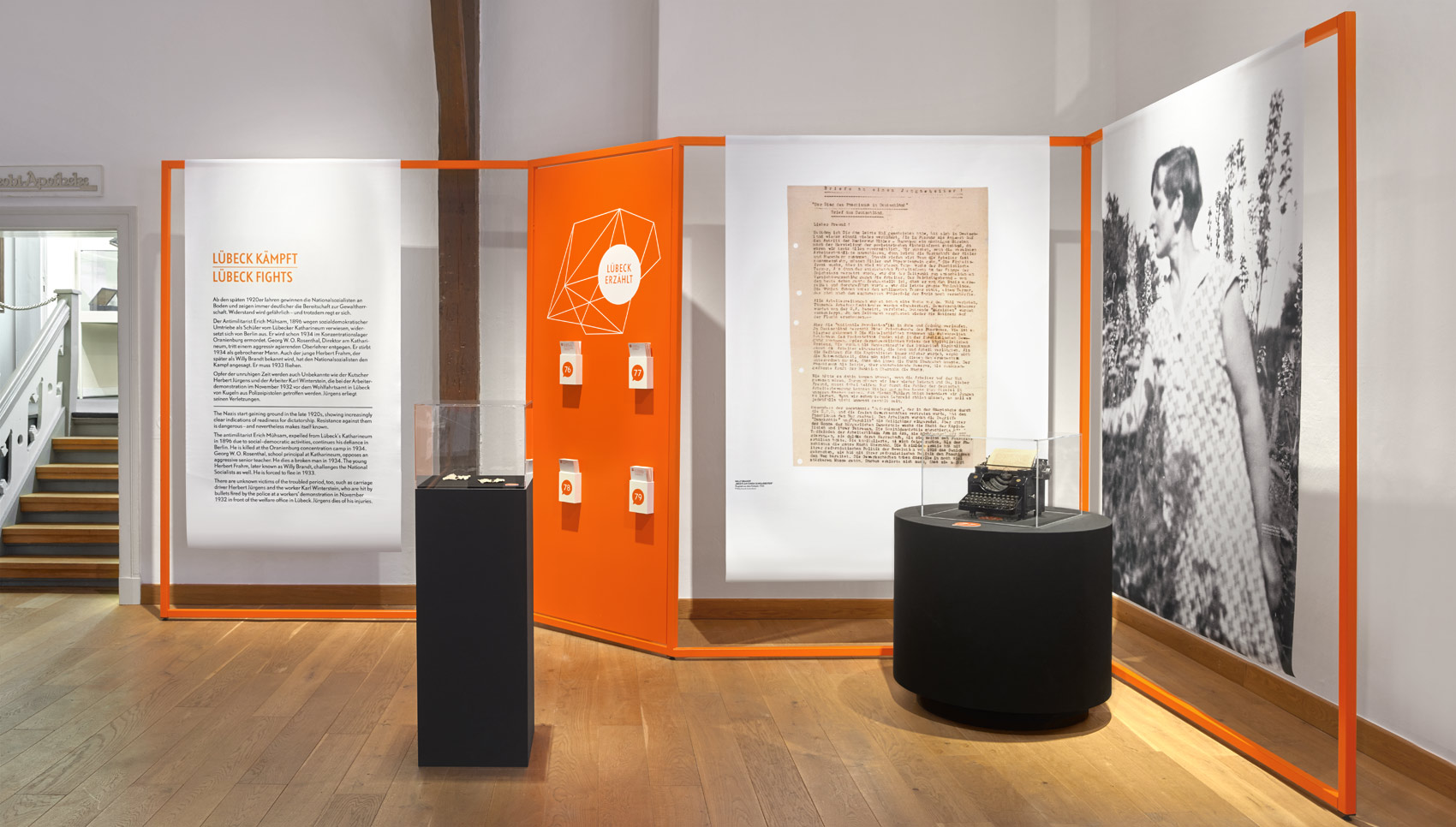 Ausstellungsraum mit Ausstellungsmöbel, bei dem Stoffbanner auf organgefarbigen Stangen hängen