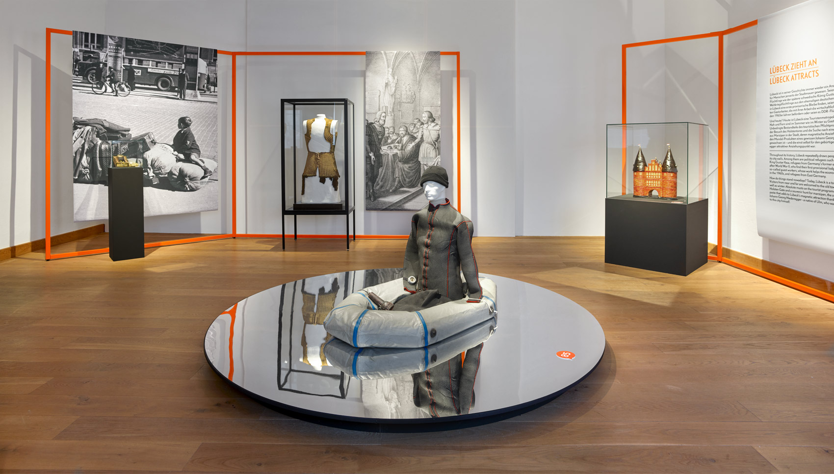 Ausstellungsraum mit Ausstellungsmöbel, bei dem Stoffbanner auf organgefarbigen Stangen hängen im Hintergrund, in der Mitte ein Exponat