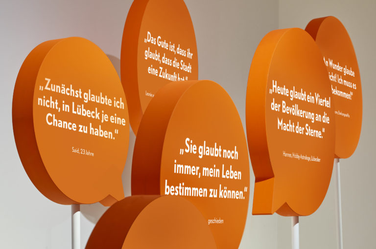 Ausstellungsgrafik mit gebauten orangenen Sprechblasen