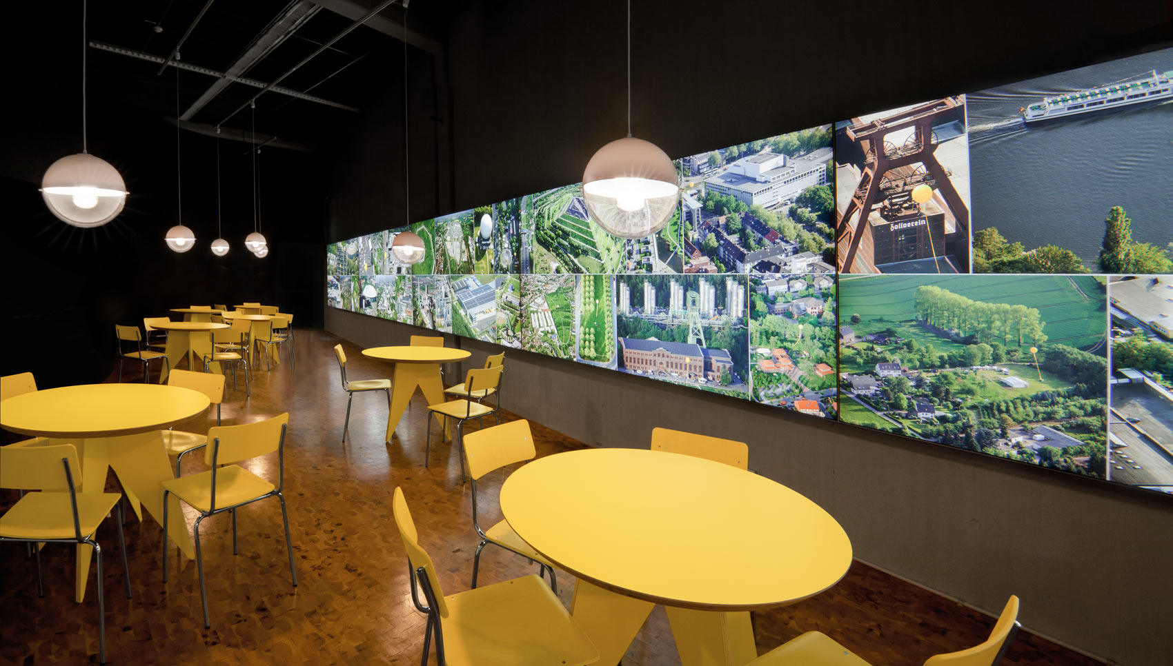 Raum mit Tischen und Stühlen und einer hinterleuchteten Ausstellungswand