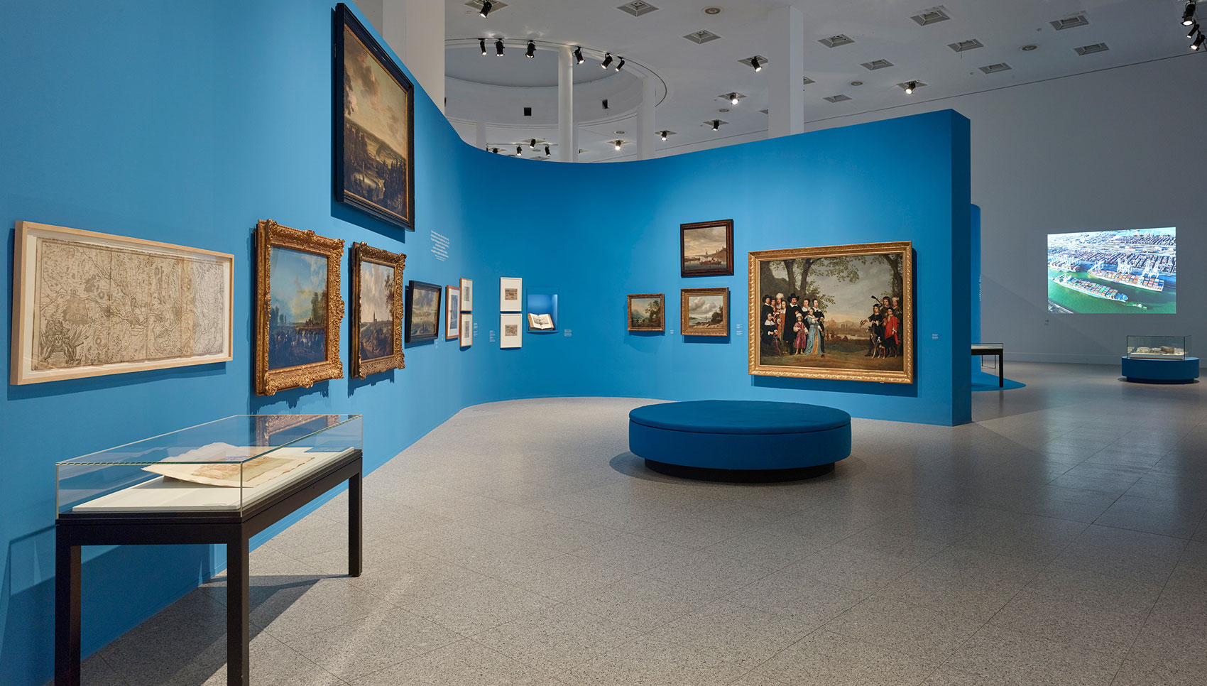 In einem blauen Ausstellungsraum hängen Gemälde und stehen Exponate.
