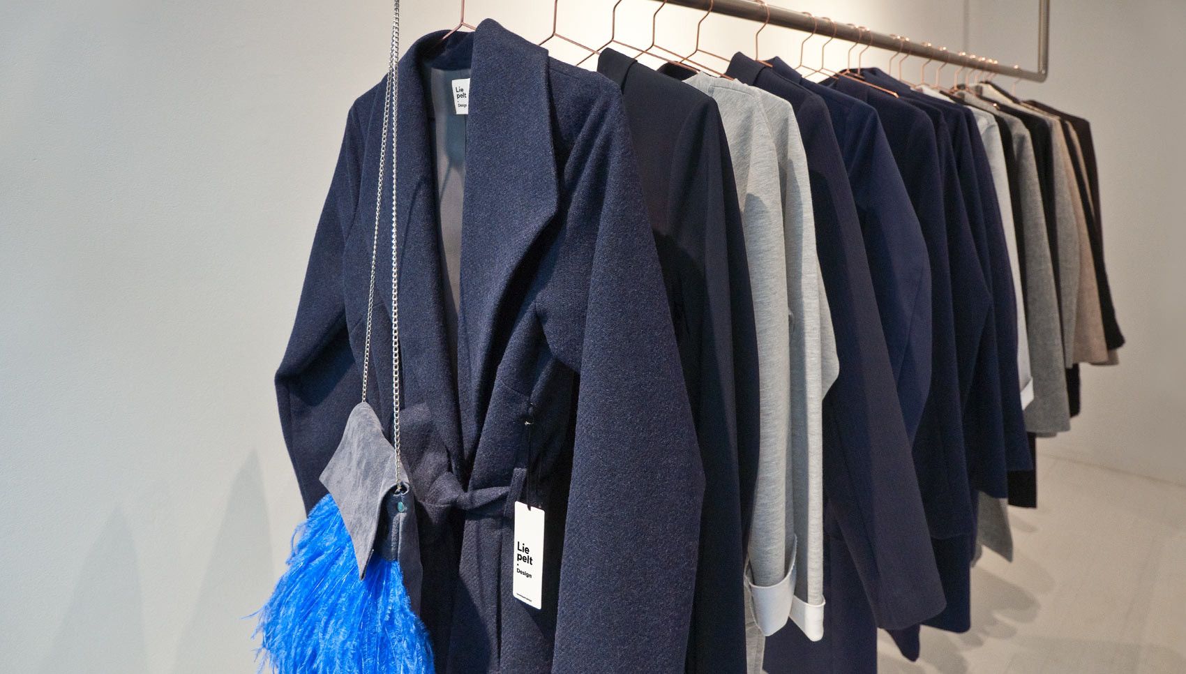 Kleiderstange mit Kleidung, im Vordergund Mantel mit Hangtag, auf dem das Logo zu sehen ist