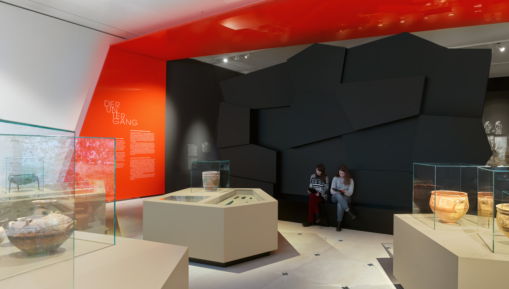 Ausstellungsraum mit Blick auf schwarze Wand mit verschiedenen Vitrinen