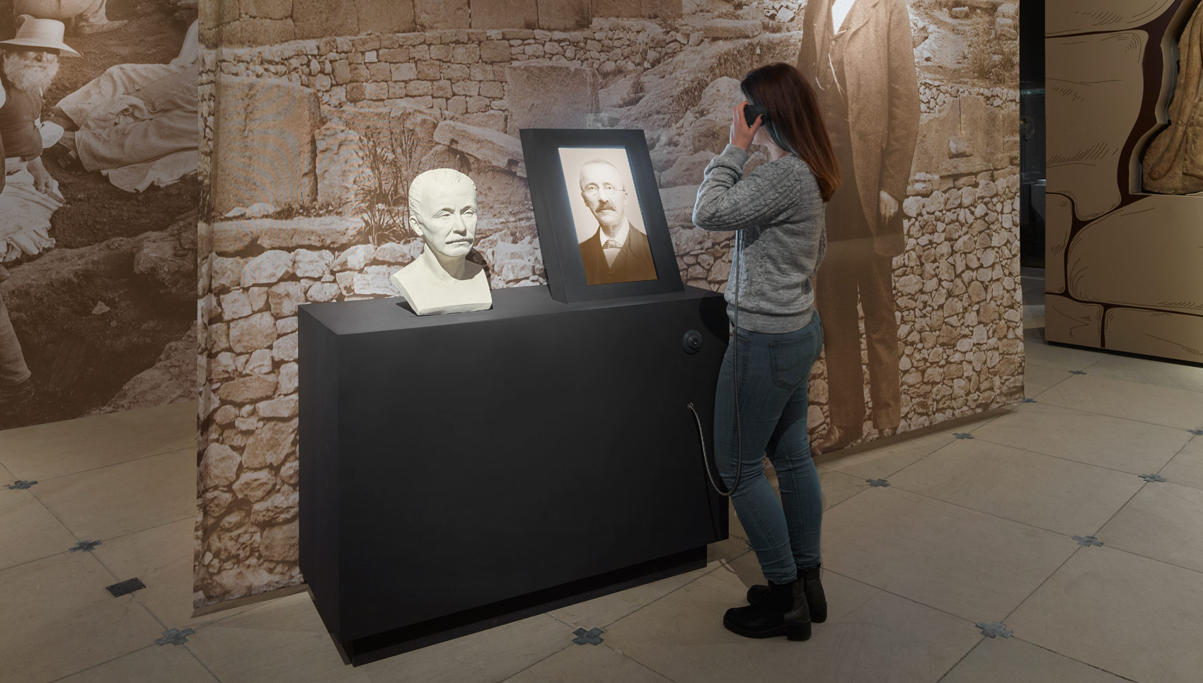 Frau steht in Ausstellungsraum und guckt und hört sich ein interaktives Exponat an