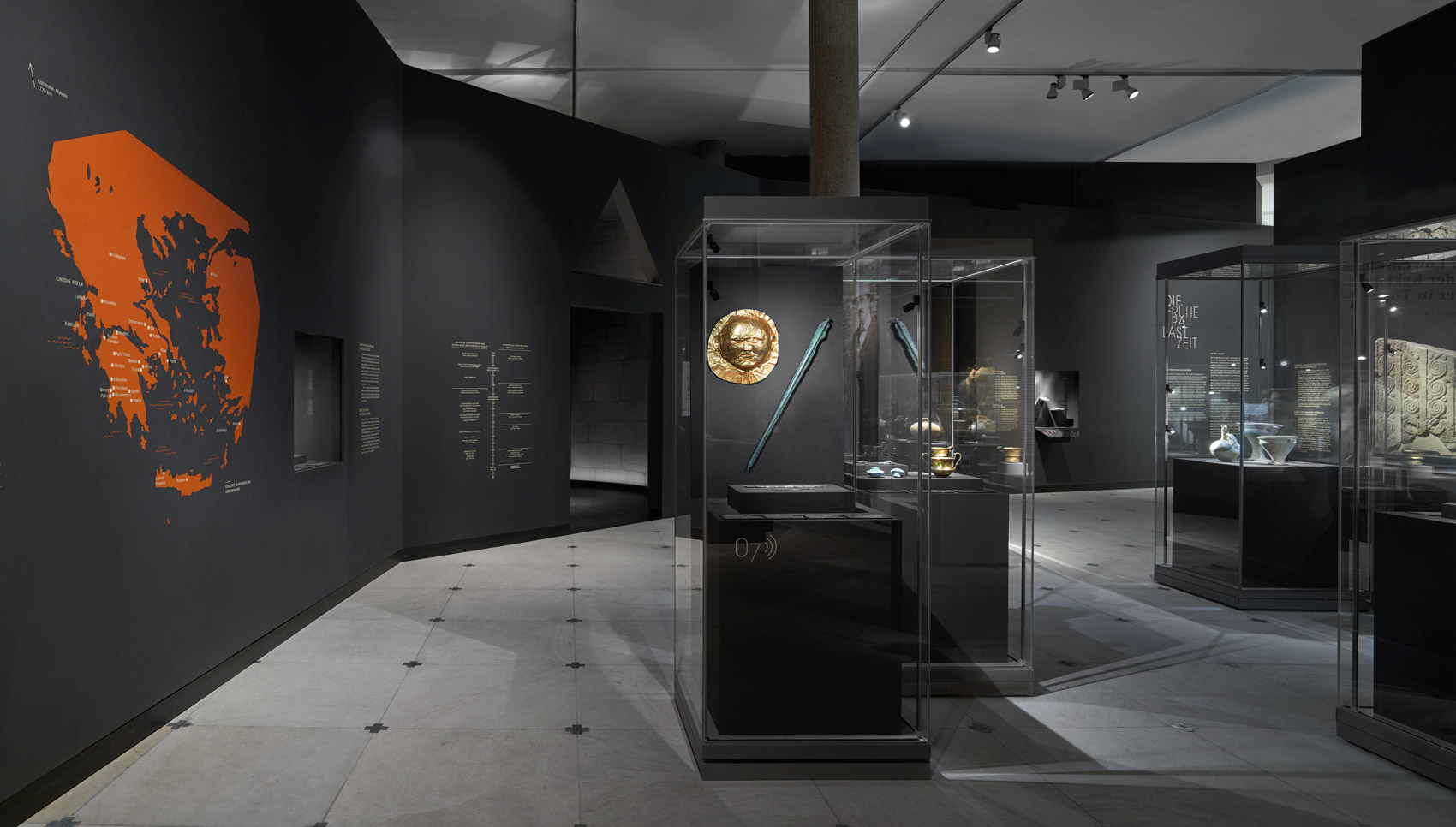 Dunkler Ausstellungsraum mit Wandgrafiken und verschiedenen Exponaten